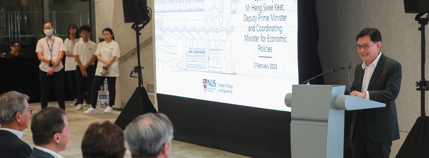 Man at podium with microphone in suit, speaking near screen for NUS event to audience.